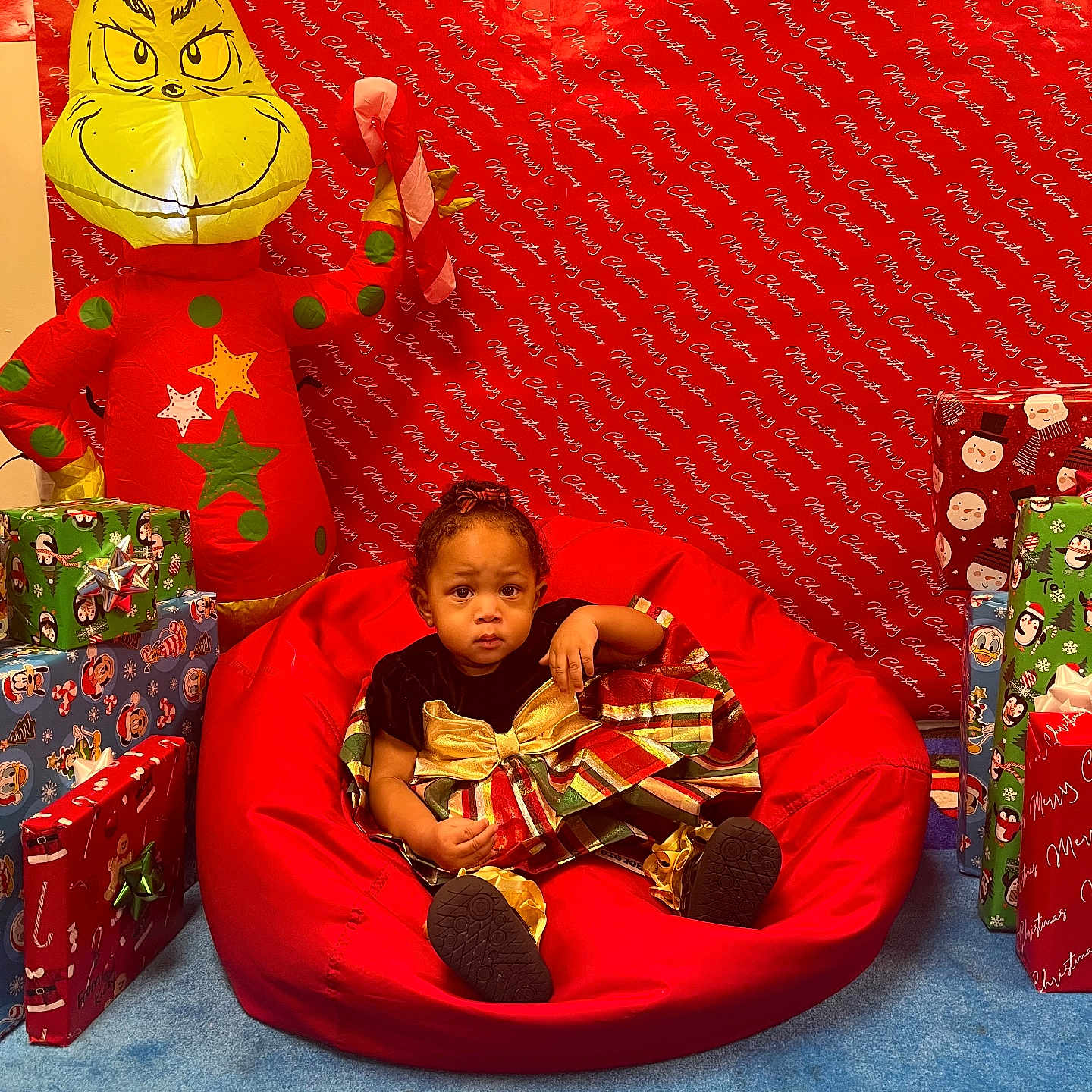 Catilayah is registered to the contest to win money with this photo: background, bean_bag, blue_carpet, candy_cane, celebration, child, christmas, christmas_theme, decorations, festive_dress, happy, holiday, indoor, inflatable_grinch, presents, red, red_backdrop, smiling_face, toddler, wrapped_gifts