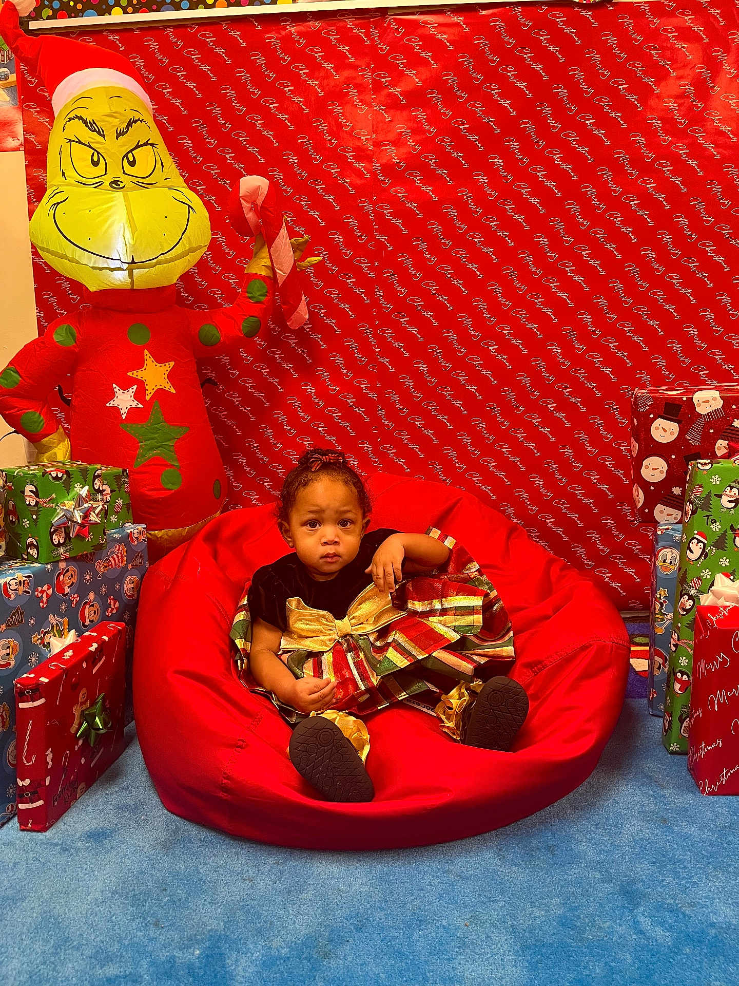 Catilayah is registered to the contest to win money with this photo: toddler, child, bean_bag, red, christmas, holiday, presents, wrapped_gifts, inflatable_grinch, candy_cane, festive_dress, blue_carpet, indoor, smiling_face, decorations, background, celebration, christmas_theme, red_backdrop, happy
