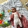 Tiya a rejoint le concours — aidez-le/la à gagner de superbes lots ! baby, infant, toy, blanket, plush_toy, floor, white_clothing, pink_vest, socks, feet, wooden_floor, happy, smiling, child, indoor, playtime, cute, lying_down, colorful, soft_toy