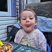 Lorena participe au concours pour gagner de l'argent avec cette photo : toddler, child, messy_face, tongue_out, unicorn_shirt, outdoor, backyard, table, fries, plate, chair, food, window, fence, trees, person, playful, casual_clothing, daylight, plastic_chair
