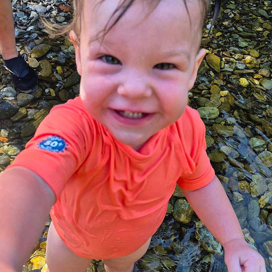 Lorena a rejoint le concours — aidez-le/la à gagner de superbes lots ! child, closeup, daylight, feet_in_water, happy, nature, orange_shirt, outdoor, person, playful, reaching_out, rocks, shallow_water, smiling, splashing, stream, summer, toddler, water, wet_hair