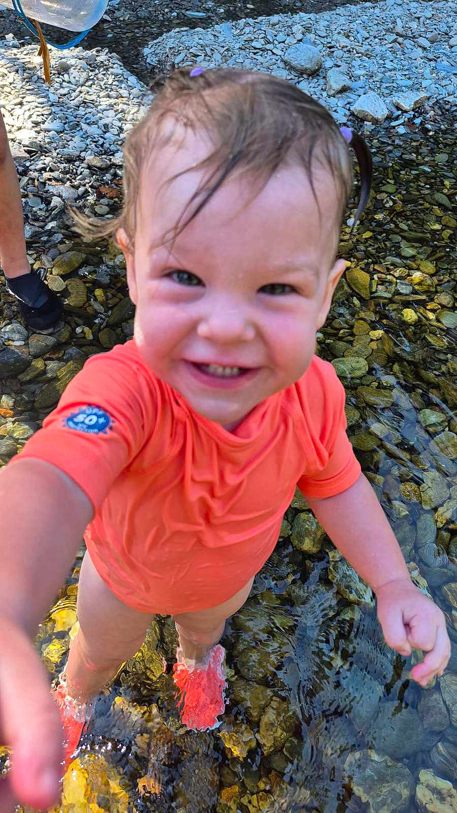 Lorena a rejoint le concours — aidez-le/la à gagner de superbes lots ! toddler, child, water, stream, rocks, orange_shirt, smiling, happy, outdoor, nature, splashing, feet_in_water, wet_hair, summer, playful, person, daylight, reaching_out, shallow_water, closeup