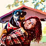 woman, dog, red_hair, plaid_shirt, outdoor, smiling, happy, pet, canine, animal, holding, park, nature, daylight, pavilion, trees, tongue_out, leisure, friendship, casual_clothing