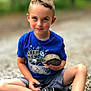 child, boy, turtle, blue_shirt, shorts, sitting, outdoor, gravel, smiling, nature, animal, casual_clothing, footwear, young, portrait, daylight, holding, cute, happy, leisure