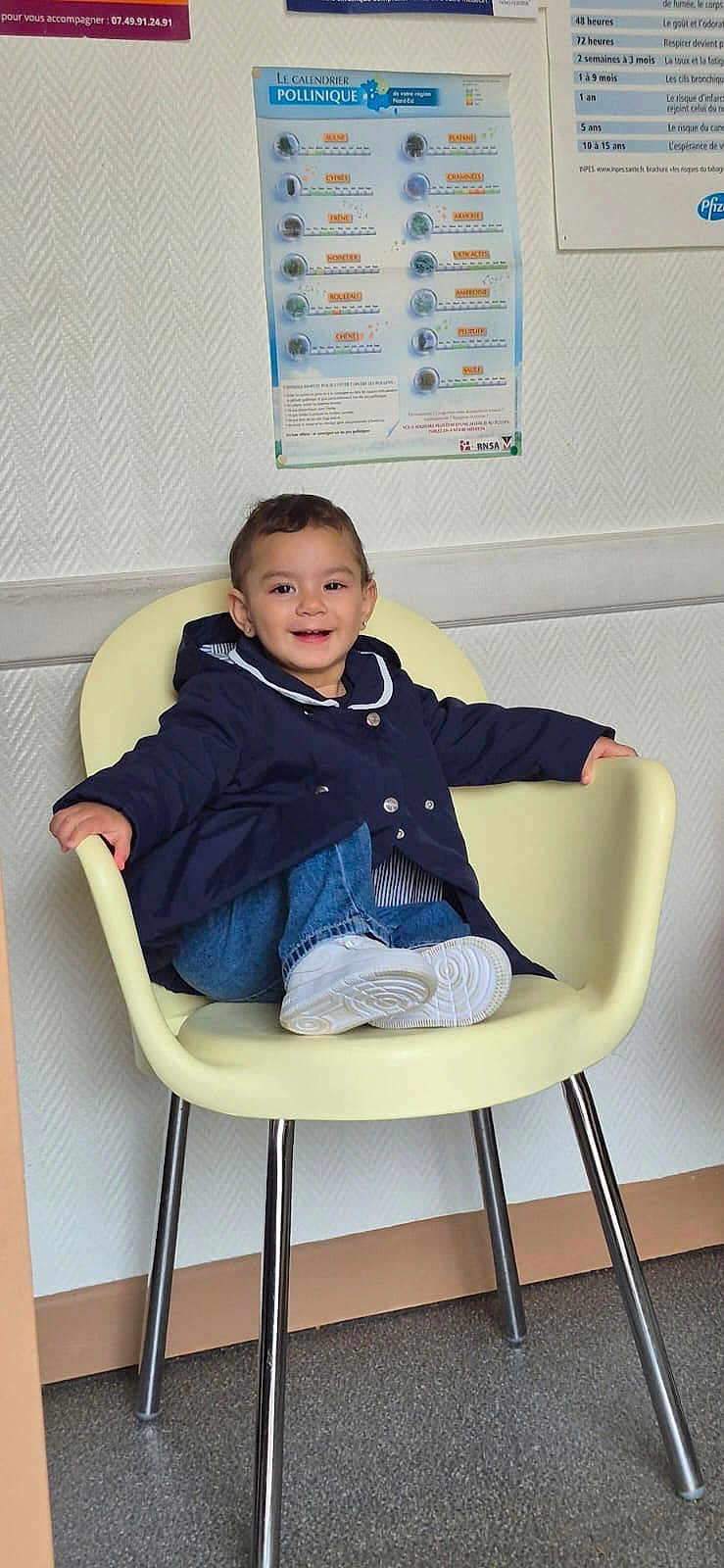 Maya a rejoint le concours — aidez-le/la à gagner de superbes lots ! child, toddler, smiling, waiting_room, chair, jacket, denim, white_shoes, sneakers, poster, wallpaper, indoor, portrait, happy, hair, legs, metal_chair_legs, floor, clinic, seated