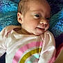 baby, blanket, child, closeup, clothing, colorful, cute, face, happy, head, indoors, infant, lying_down, newborn, onesie, person, portrait, rainbow, smiling, soft_texture