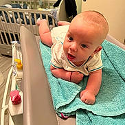 Evan participe au concours pour gagner de l'argent avec cette photo : baby, infant, changing_table, towel, nursery, crib, plush_toys, diaper, white_clothing, floor, wooden_floor, door, baby_care, child, indoor, room, person, skin, head, expression