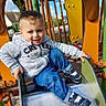 child, boy, slide, playground, outdoor, smiling, hoodie, jeans, sneakers, play, fun, daylight, happy, recreation, park, metal_slide, handrails, casual_clothing, young, active