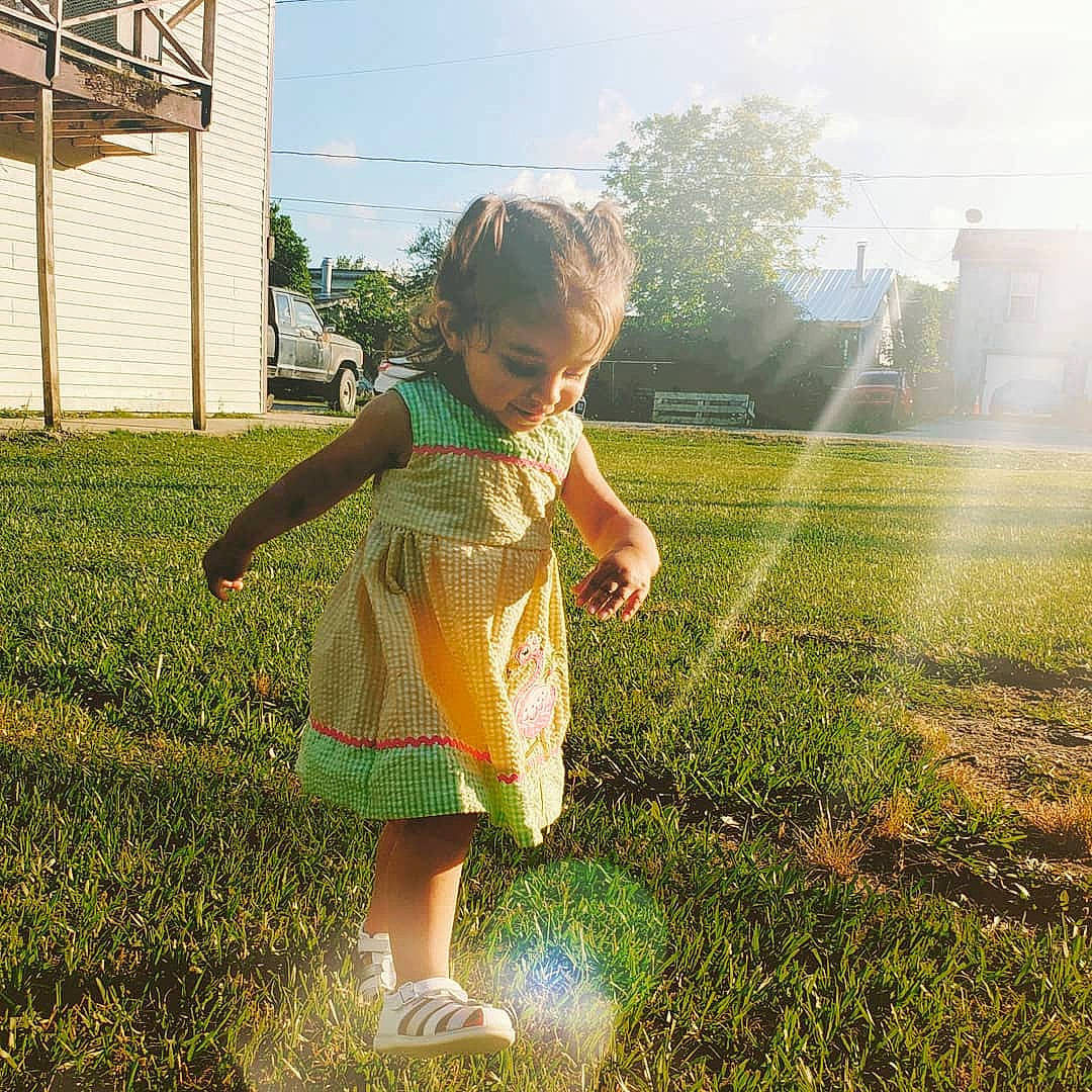 Emma is registered to the contest to win money with this photo: backlighting, child, dress, fun, grass, grass_family, green, happy, lawn, morning, people_in_nature, person, play, sky, smile, spring, summer, sunlight, toddler, tree