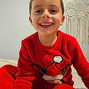 Maël a rejoint le concours — aidez-le/la à gagner de superbes lots ! child, boy, smiling, red_pajamas, christmas_theme, face, happy, indoors, macrame, wall_hanging, cozy, portrait, cute, sitting, home, holiday, clothing, young, bright, warm
