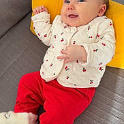 Lila participe au concours pour gagner de l'argent avec cette photo : baby, infant, smiling, yellow_pillow, grey_couch, red_pants, white_jacket, cherry_pattern, socks, slippers, hands, eyes, portrait, cozy, home_interior, fabric, cushion, happy, seated, cute