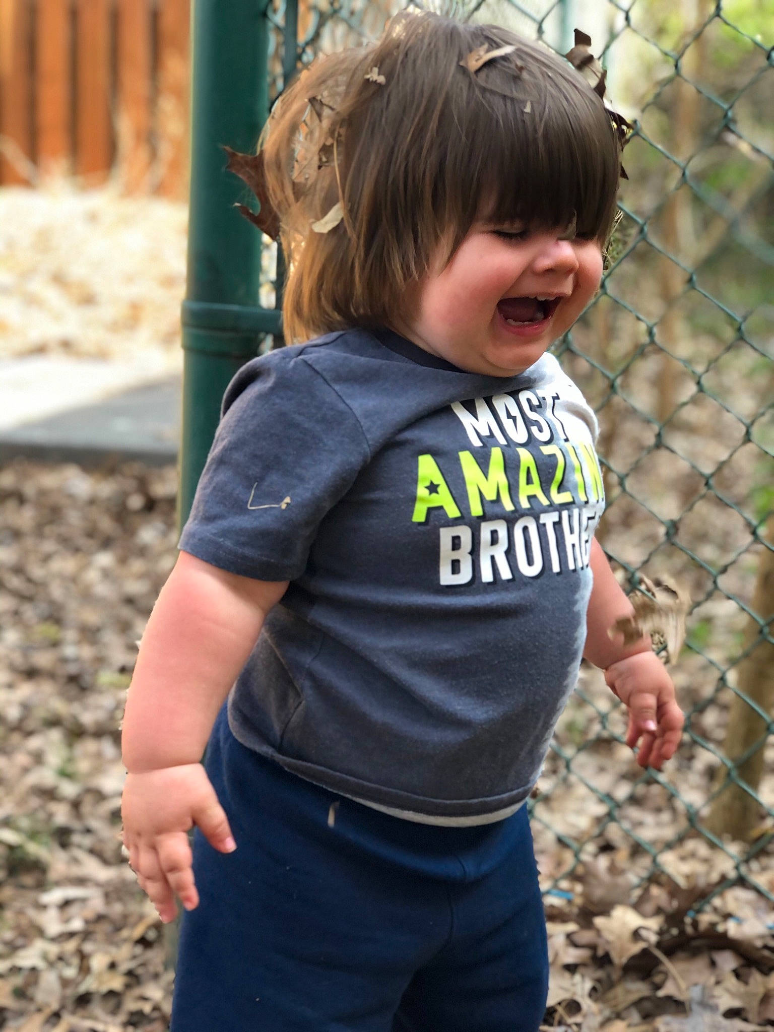 Winston is registered to the contest to win money with this photo: clothing, fence, grass, hair, hairstyle, happy, head, joy, leaf, leisure, mesh, people_in_nature, person, photograph, plant, recreation, sleeve, smile, t_shirt, toddler
