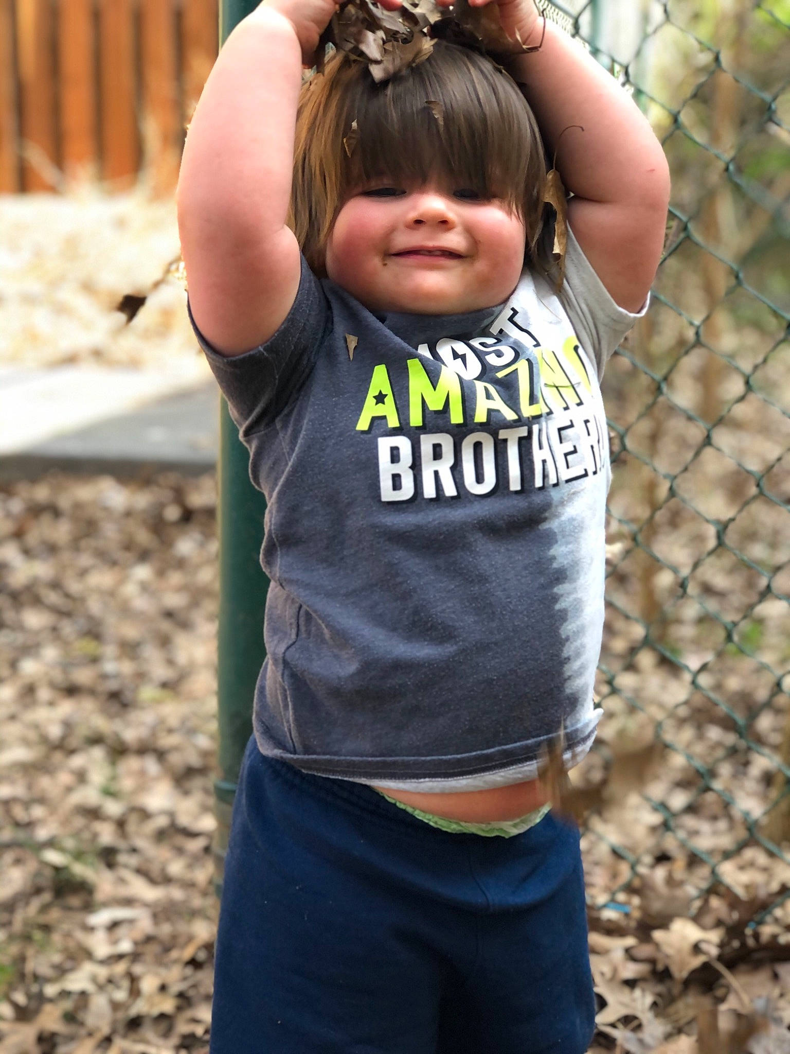 Winston is registered to the contest to win money with this photo: baby_toddler_clothing, child, face, fence, fun, grass, happy, joy, leisure, mesh, outdoor_play_equipment, people_in_nature, person, personal_protective_equipment, recreation, sleeve, smile, soil, swing, t_shirt