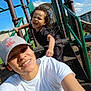 Marcus is registered to the contest to win money with this photo: child, adult, playground, slide, stairs, railing, curly_hair, smiling, selfie, hat, t_shirt, tattoo, outdoors, blue_sky, park, playground_equipment, metal_posts, happy, person, play