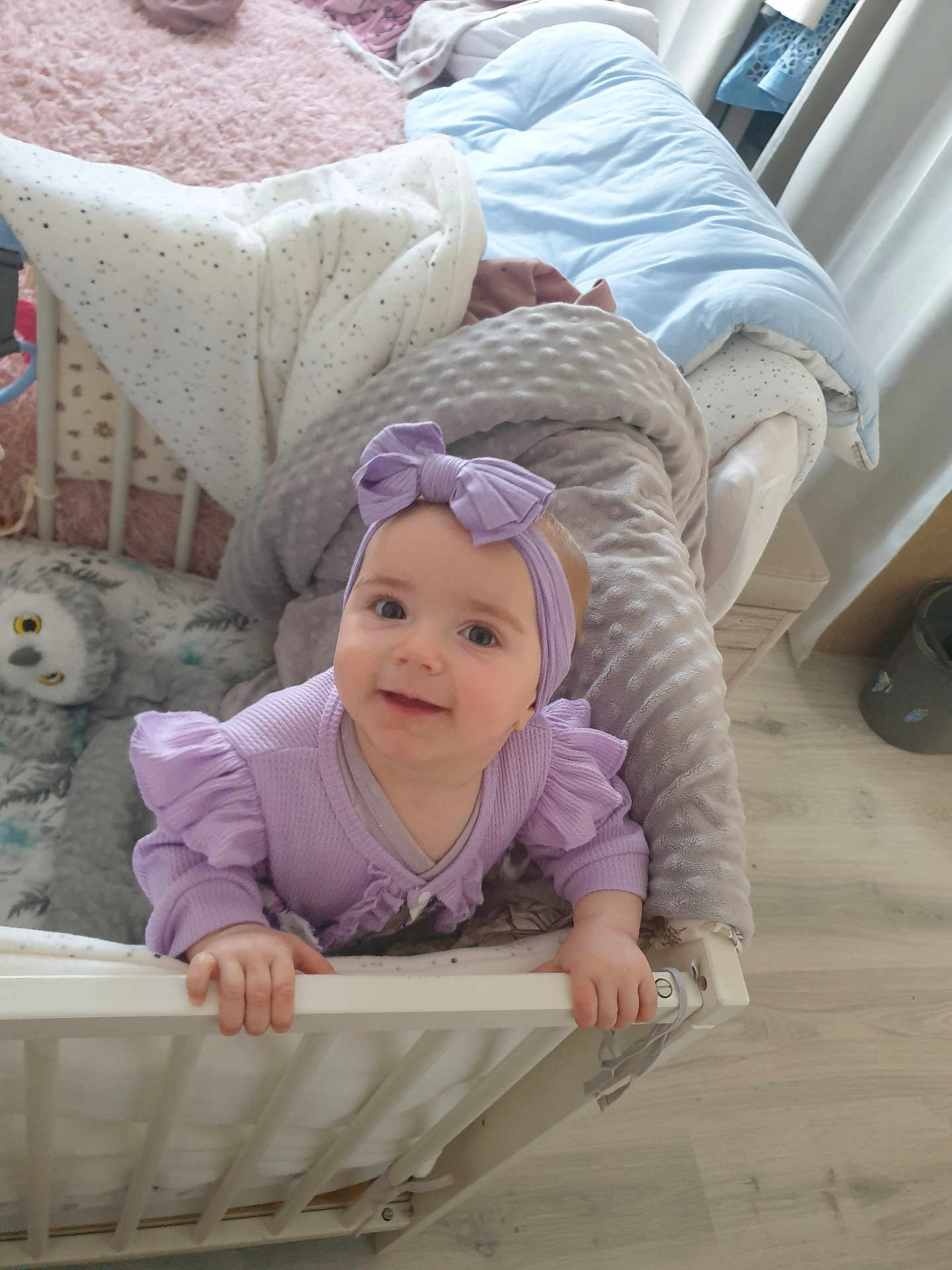 Cassie participe au concours pour gagner de l'argent avec cette photo : baby, infant, crib, blanket, stuffed_animal, owl, headband, purple_clothing, smiling, indoors, nursery, wooden_floor, child, person, handrail, bedroom, cute, toddler, happy, soft_toys