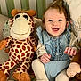 baby, child, smiling, stuffed_animal, giraffe, plush_toy, blue_dress, white_tights, curly_hair, happy, indoor, seated, cushion, soft_toys, playroom, portrait, cute, infant, cozy, home