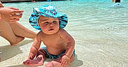 Zion joined the competition — help win amazing prizes! baby, child, infant, swimming_pool, resort, outdoor, tropical, palm_trees, sunhat, swimwear, water, sitting, smiling, portrait, family, vacation, sunlight, shallow_water, poolside, people