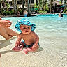 baby, child, infant, swimming_pool, resort, outdoor, tropical, palm_trees, sunhat, swimwear, water, sitting, smiling, portrait, family, vacation, sunlight, shallow_water, poolside, people