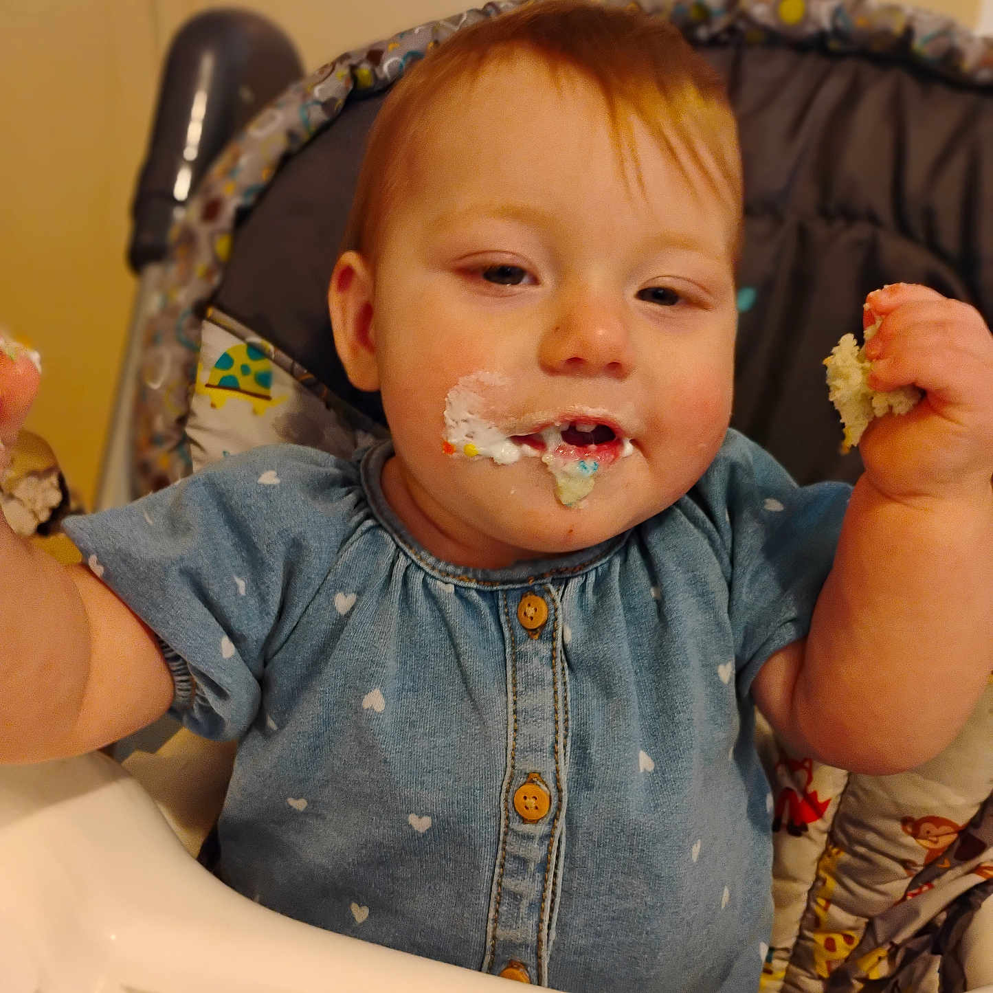 Blanche is registered to the contest to win money with this photo: baby, blue_dress, cake, cheeks, child, crumbs, cute, eating, face, food, frosting, hands, happy, heart_pattern, high_chair, indoor, infant, messy, person, smiling