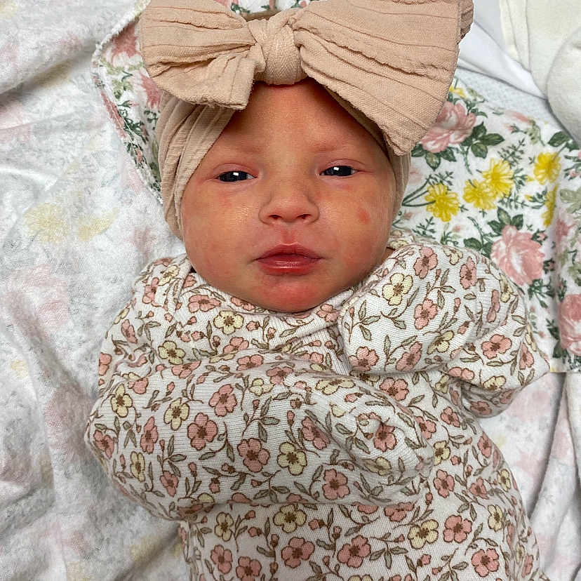 Paislee is registered to the contest to win money with this photo: newborn, baby, headband, bow, floral_pattern, blanket, infant, clothing, sleepwear, cute, small_face, wrapped, soft, lying_down, indoors, portrait, baby_girl, fabric, texture, resting