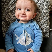 Logan is registered to the contest to win money with this photo: baby, blanket, blue_onesie, child, clothing, cozy, cute, expression, face, hand, happy, indoor, infant, lying_down, person, portrait, shark_design, smiling, texture, young_child