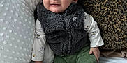 Logan joined the competition — help win amazing prizes! baby, child, infant, smiling, face, vest, green_pants, socks, pillow, blanket, bed, cute, indoors, cozy, plush, person, portrait, sitting, happy, home