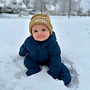 Logan joined the competition — help win amazing prizes! baby, child, snow, winter, outdoor, cold, blue_snowsuit, beanie, hat, cute, smiling, sitting, snowy_background, face, person, clothing, seasonal, cold_weather, fun, playful