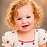 toddler, child, smile, curly_hair, blue_eyes, dress, white_clothing, apple_pattern, portrait, happy, cute, innocence, outdoor, soft_background, close_up, young_child, puffy_sleeves, red_embroidery, cheerful, face