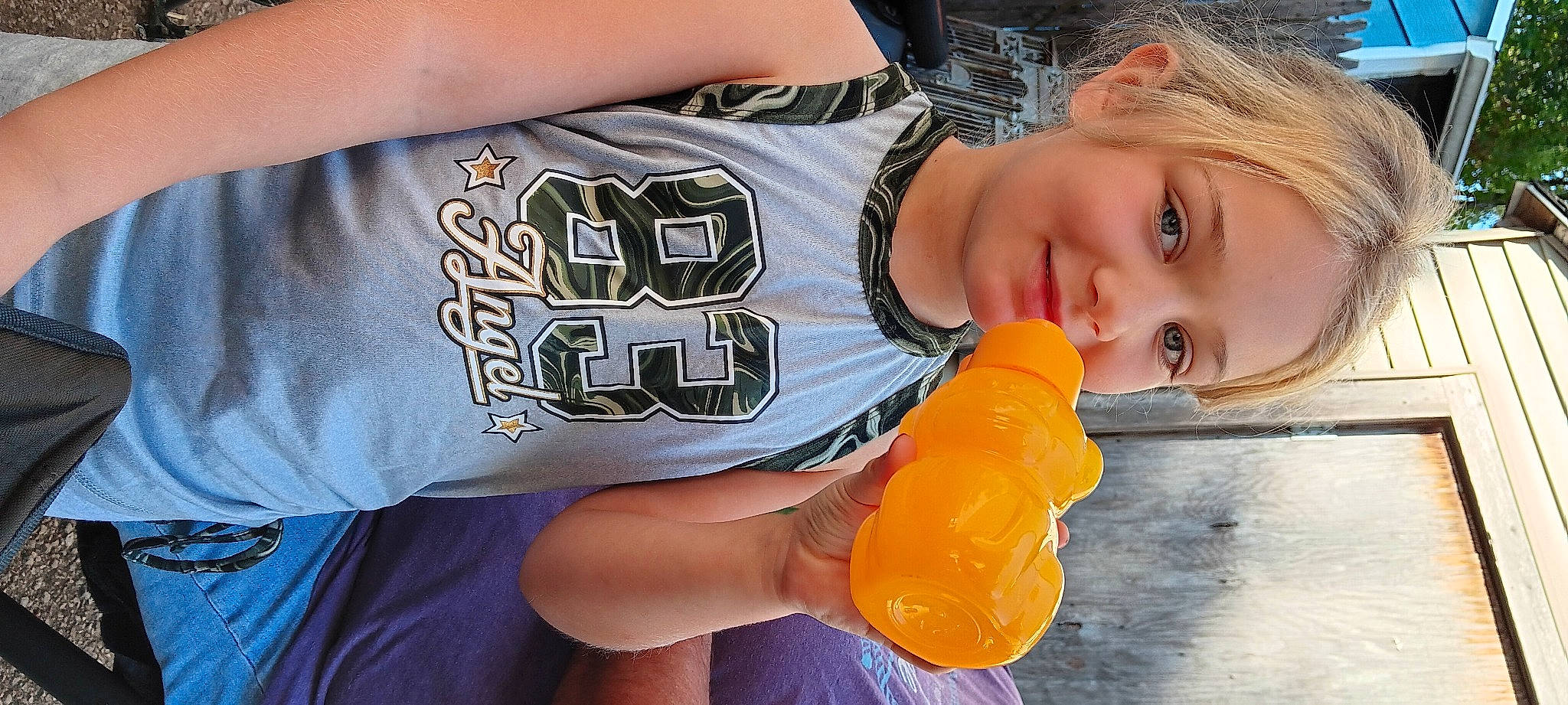 Dixie is registered to the contest to win money with this photo: chest, child, drink, drinkware, elbow, electric_blue, finger, fun, gesture, happy, human_leg, joy, nail, orange, person, plastic_bottle, sleeve, t_shirt, thigh, thumb