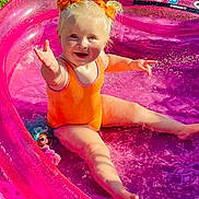 Darcey joined the competition — help win amazing prizes! toddler, child, pool, pink, inflatable, water, outdoor, sunlight, orange_swimsuit, hair_bows, smiling, splashing, toy_doll, grass, summer, playtime, happy, cute, barefoot, fun