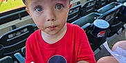 Colton is registered to the contest to win money with this photo: baseball_stadium, cap, child, crowd, curious, daylight, drink_bottle, event, facial_expression, hat, mickey_mouse, outdoor, people, plastic_bottle, red_shirt, seating, spectator, sports, toddler, toy_topper