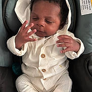 Alijah is registered to the contest to win money with this photo: baby, infant, white_outfit, hooded_jacket, car_seat, pacifier, hand, curly_hair, wooden_buttons, socks, sitting, child, warning_label, safety, indoor, cute, small_fingers, clothing, seat, portrait