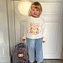Nina participe au concours pour gagner de l'argent avec cette photo : child, smiling, indoor, door, backpack, sweatshirt, striped_pants, checkered_shoes, floor, light, shadow, blond_hair, young_child, standing, casual_clothing, happy, blue_eyes, portrait, home, person