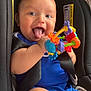 baby, blue_clothing, car_seat, cheerful, child, close_up, colorful, cute, fun, happy, holding, indoor, infant, person, playful, seat, seatbelt, smiling, tongue_out, toy