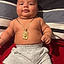 baby, infant, child, gold_chain, bracelet, shorts, socks, bed, pillow, striped_pillow, red_blanket, skin, face, chubby, smiling, lying_down, indoors, cute, jewelry, comfort