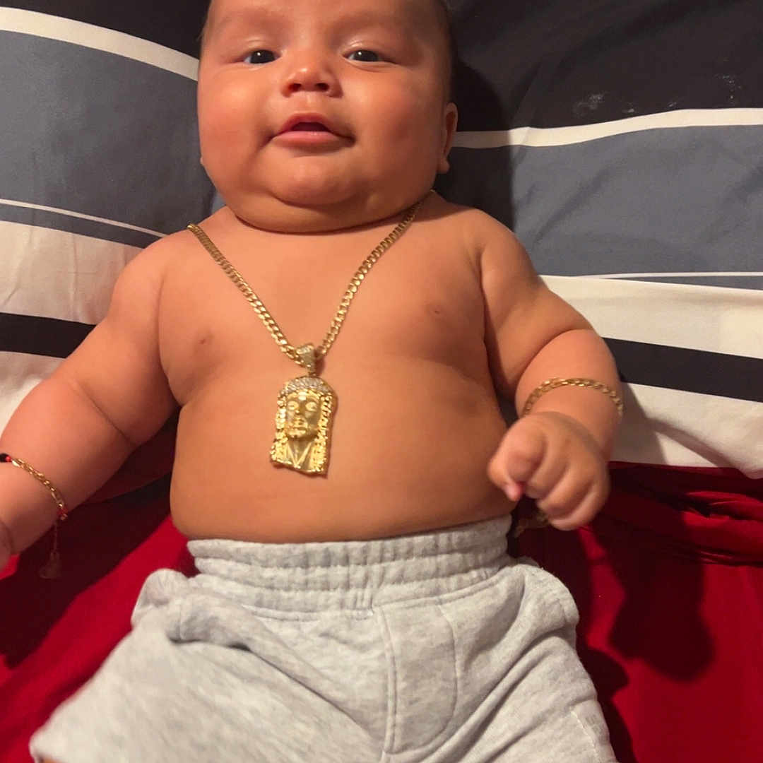 Krisniel is registered to the contest to win money with this photo: baby, bed, bracelet, child, chubby, comfort, cute, face, gold_chain, indoors, infant, jewelry, lying_down, pillow, red_blanket, shorts, skin, smiling, socks, striped_pillow