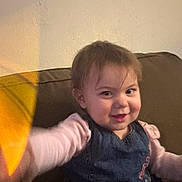 Aryella joined the competition — help win amazing prizes! toddler, child, smile, face, couch, indoor, clothing, denim, pink_sleeves, hair, happy, young_child, person, portrait, seated, wall, warm_light, reaching_hand, casual, home