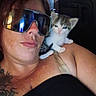 person, sunglasses, kitten, cat, shoulder, tattoo, indoor, window, reflection, face, pet, animal, young_cat, black_clothing, skin, portrait, closeup, feline, cute, relaxed