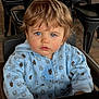 child, toddler, blue_eyes, light_brown_hair, hoodie, bear_pattern, high_chair, indoor, curious_expression, face, seated, clothing, person, furniture, metal_chair, brick_floor, portrait, casual, young_child, cute