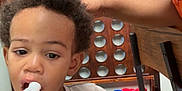 Kaizir joined the competition — help win amazing prizes! toddler, child, drinking, bottle, curly_hair, tshirt, dinosaurs, football_helmets, hand, adult, glasses, braids, game_board, wooden, chair, table, indoor, person, face, casual
