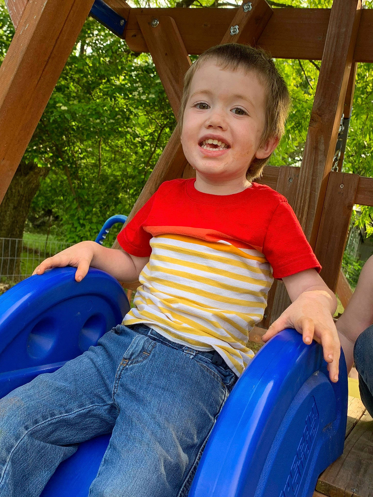 Joseph is registered to the contest to win money with this photo: baby_toddler_clothing, blue, facial_expression, finger, fun, grass, happy, jeans, joy, lap, leisure, outdoor_play_equipment, person, playground, recreation, shorts, skin, smile, t_shirt, thigh