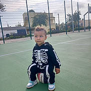 Soulaiman Jirari participe au concours pour gagner de l'argent avec cette photo : child, toddler, basketball, sports_court, outdoor, sneakers, skeleton_costume, fence, daylight, building, tree, playing, curious, casual_clothing, person, recreation, green_surface, sport, bench, shadow