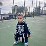 child, toddler, basketball, sports_court, outdoor, sneakers, skeleton_costume, fence, daylight, building, tree, playing, curious, casual_clothing, person, recreation, green_surface, sport, bench, shadow