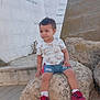 Soulaiman Jirari participe au concours pour gagner de l'argent avec cette photo : child, toddler, rock, outdoor, stone_wall, trees, shorts, shirt, sneakers, socks, person, nature, daylight, curly_hair, casual_clothing, seated, ground, expression, paw_patrol, side_view