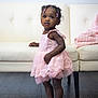 Jaya joined the competition — help win amazing prizes! toddler, child, dress, pink_dress, sandals, floor, wooden_floor, couch, furniture, blanket, pink_blanket, indoor, person, cute, standing, beads, hair_accessories, wall, white_wall, curious