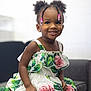 Yara is registered to the contest to win money with this photo: child, girl, smile, dress, flowers, beads, hair, braids, couch, indoor, portrait, happy, cute, fashion, sitting, young, person, skin, apparel, furniture
