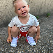 Emily participe au concours pour gagner de l'argent avec cette photo : toddler, child, smiling, squatting, blue_eyes, white_tshirt, red_shorts, white_shoes, nike, outdoor, pebbled_ground, short_hair, happy, casual_clothing, person, cute, young_child, small_food, earrings, daylight