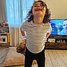 Angelo a rejoint le concours — aidez-le/la à gagner de superbes lots ! child, dog, laughing, smiling, indoors, living_room, standing, portrait, curly_hair, striped_shirt, black_pants, television, cushion, floor, curtains, window, furniture, home, pet, playful