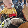 Sylas is registered to the contest to win money with this photo: baby, pacifier, bib, child, highchair, indoor, people, legs, wooden_floor, table, chair, clothing, toy, person, seated, casual, infant, cute, curious, family