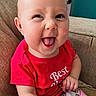 baby, child, smiling, tongue_out, red_shirt, sitting, couch, indoor, face, happy, person, patterned_pants, furniture, head, skin, cute, young_child, portrait, clothing, infant